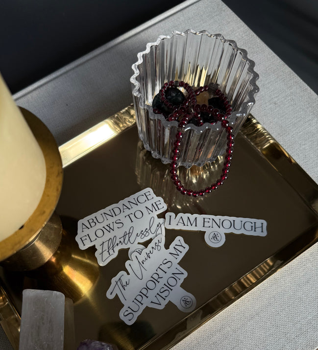 Decorative tray with motivational phrases, crystals, and a glass container on a textured surface.