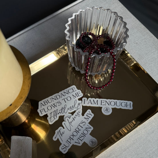 Decorative tray with motivational phrases, crystals, and a glass container on a textured surface.