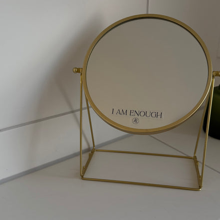 Gold-framed mirror with 'I AM ENOUGH' affirmation sticker  on the surface.