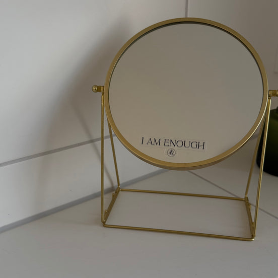 Gold-framed mirror with 'I AM ENOUGH' affirmation sticker  on the surface.