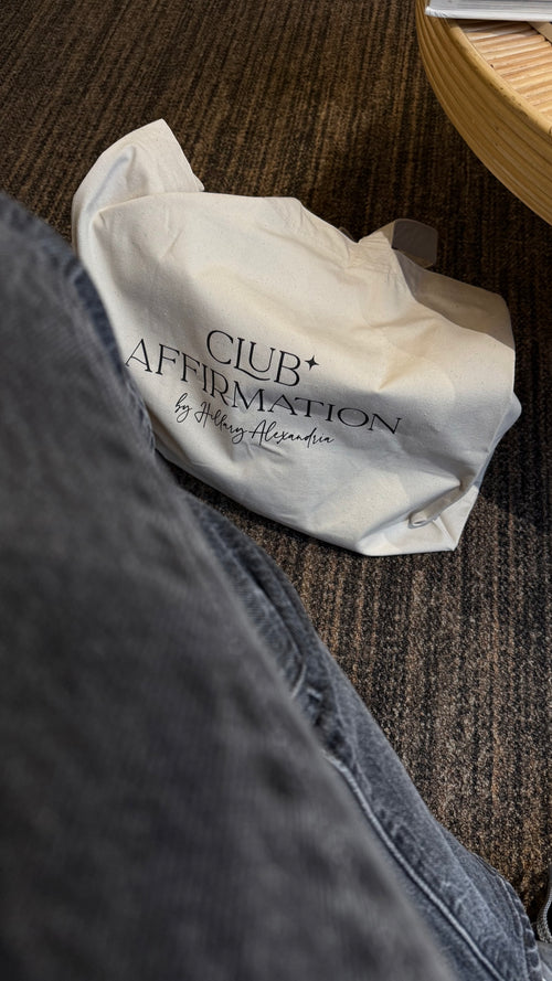 White tote bag with 'Club Affirmation' text on a textured surface