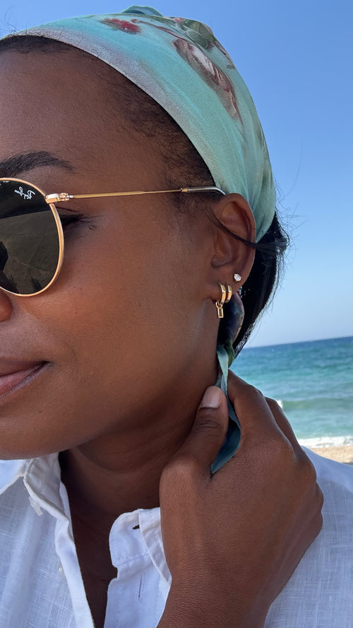 Woman wearing sunglasses and a headscarf with a beach in the background