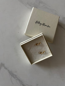 Two gold rings in a box with 'Hilary Alexander' branding on a marble surface.