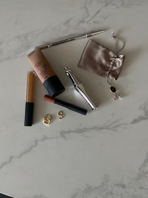 Makeup products including a brush, compact, and small pouch on a marble surface