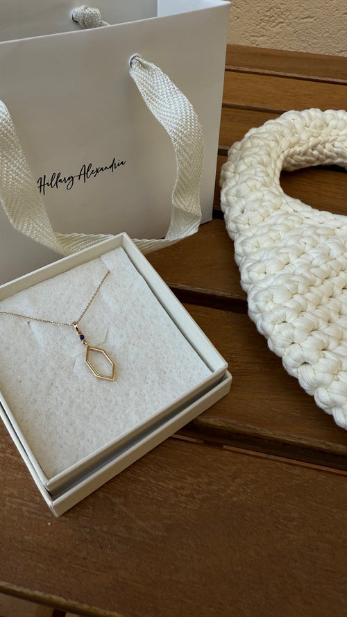 Gold necklace in a box with a branded bag in the background on a wooden surface